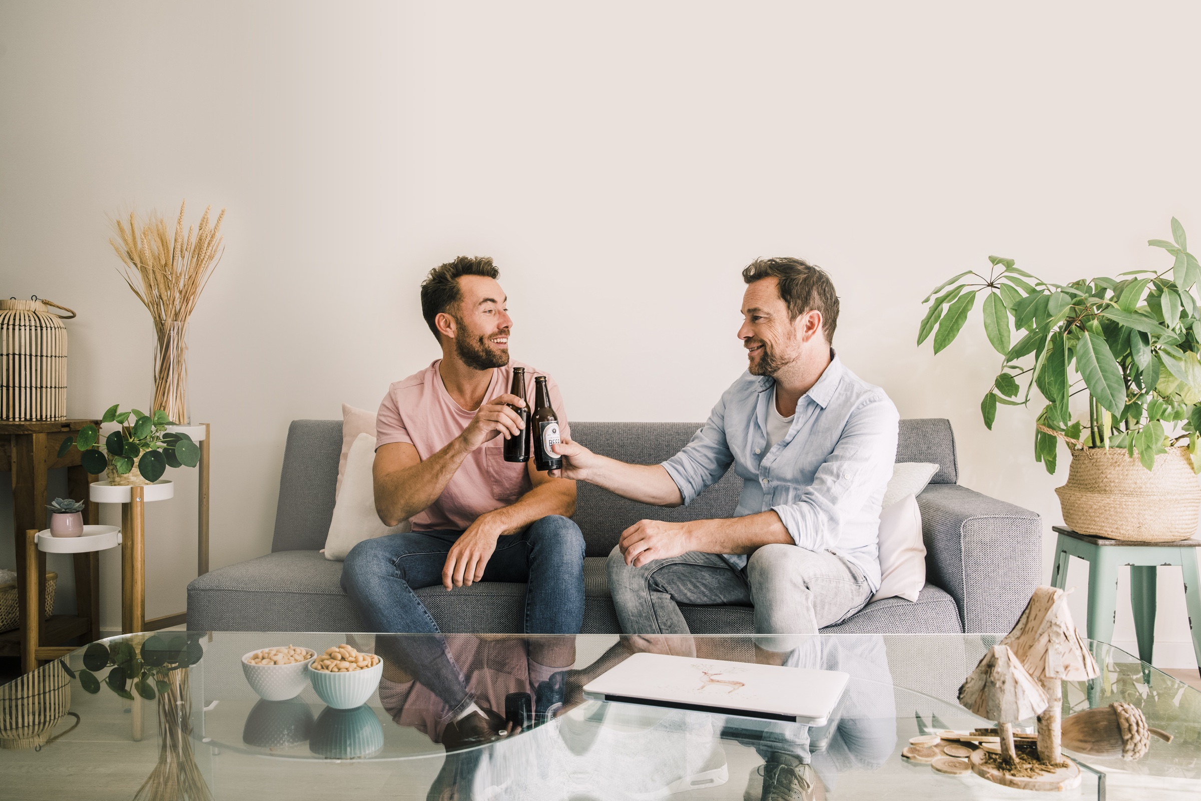Twee mannen op de bank proosten met een flesje bier.